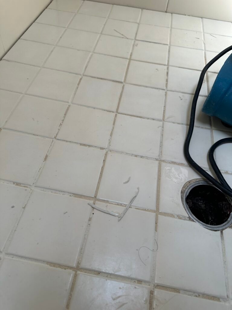 Close-up of peeling grout colorant on shower floor discovered during the scrubbing process.